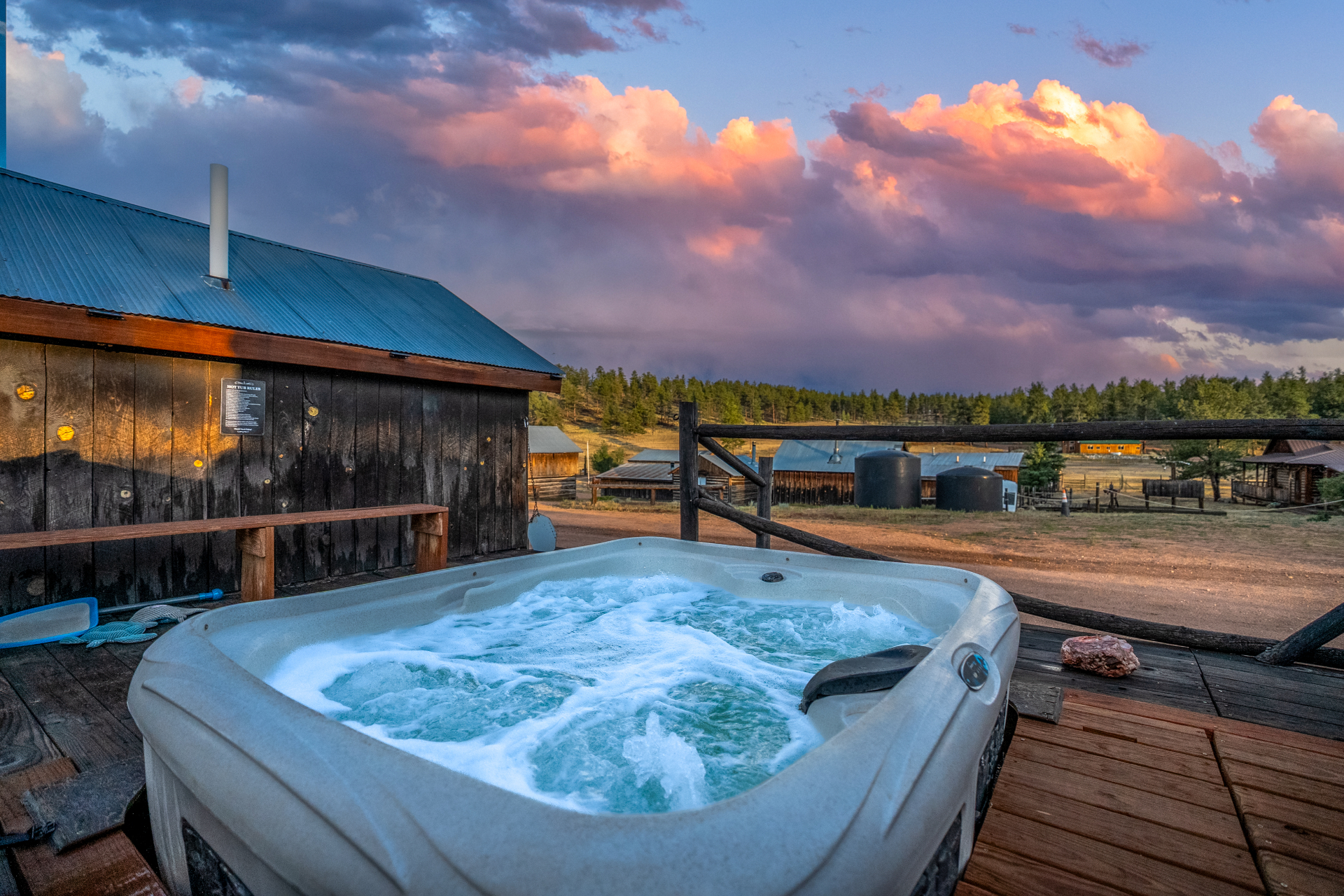 Outdoor hot tub on a wooden deck at M Lazy C Ranch beneath a pink cloud sunset